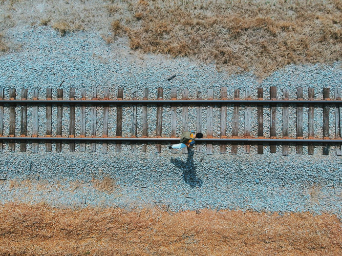 A birds eye view camera angle of a man walking along traintracks