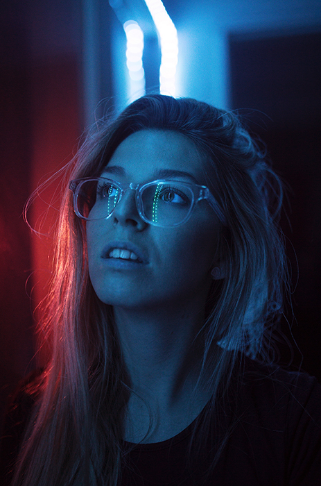 An atmospheric neon photography portrait of a female model with neon lights reflected in her glasses